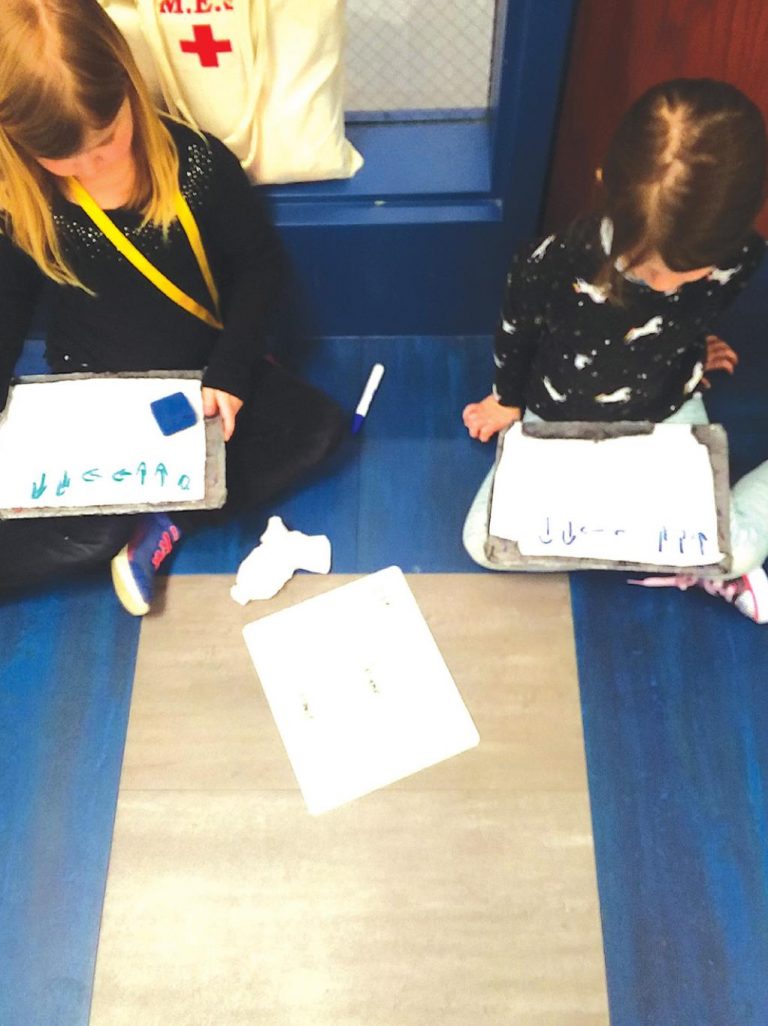 Maggie Terrill, right, first programmed her code sequence down on paper to navigate Avah Jackson to move the correct amount of spaces for the cat to get to the mouse then to the house. Avah followed the code sequence given by moving her finger on the board, and then rewriting the code herself. SUBMITTED PHOTO