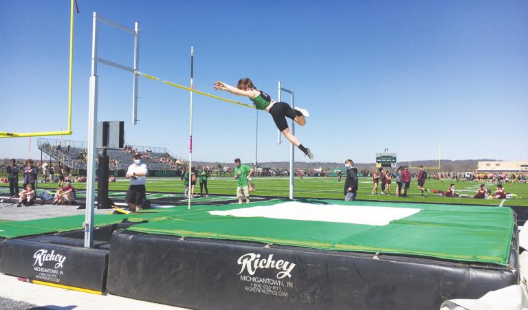 Harrison’s Kyle Hater, above, clears the bar on a pole vault during Harrison’s all-comers meet Saturday. Senior Shaunti Tolliver, at left, warms up for the shot put competition, which she would win. PHOTOS BY DICK MALONEY