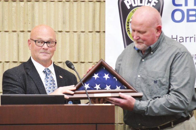 Police Officer Joe Willig accepts the flag that flew over the Harrison Police Department May 28, the day he retired. Presenting the flag is Mayor Bill Neyer. HALIE BARGER/THE HARRISON-PRESS